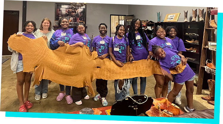 A group of young girls pose for a photo holding a leather hide from an alligator.